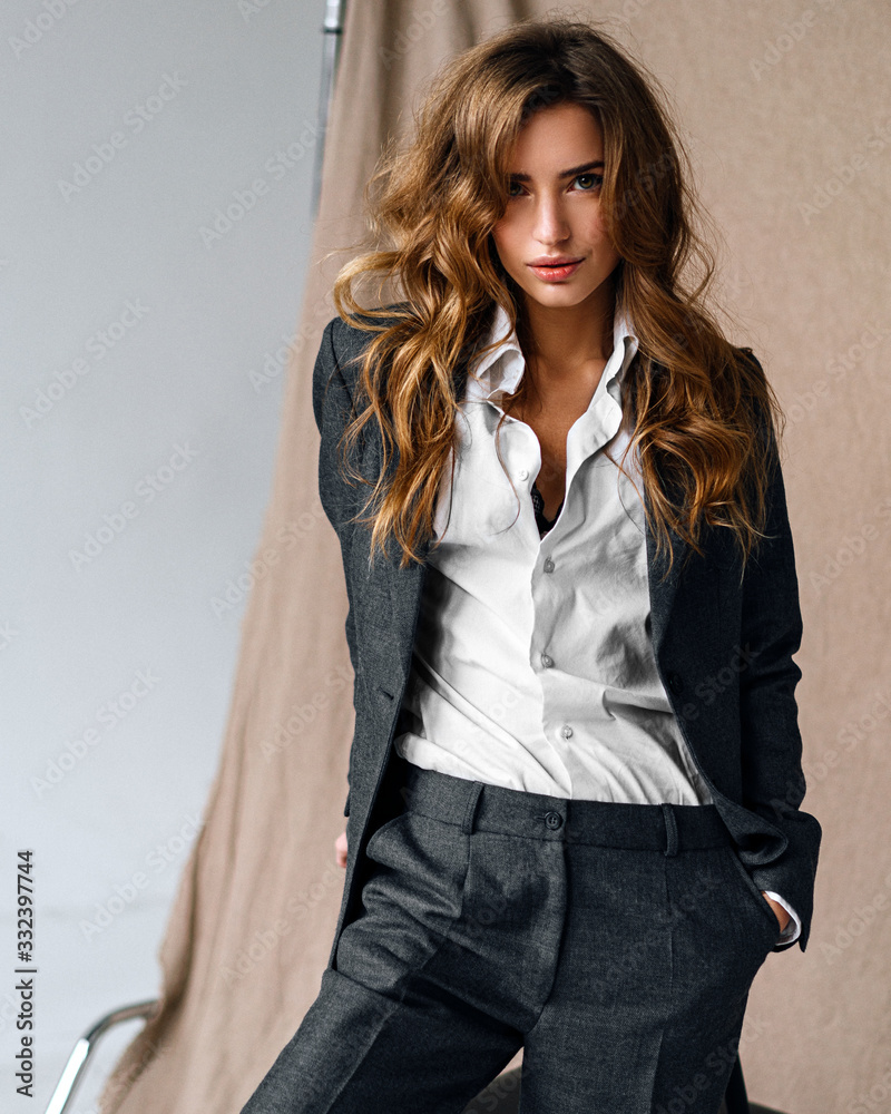 Fashion woman portrait in classic suit, white shirt posing near chair. Stylish elegant model posing loft studio Fashion woman portrait in classic suit, white shirt posing near chair. Stylish elegant model posing loft studio