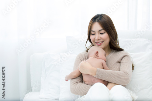Beautiful mom supports and tenderly cuddles the newborn baby gently while the infant is sleeping on the chest. Asian mother looking at the baby with love and showing protection.