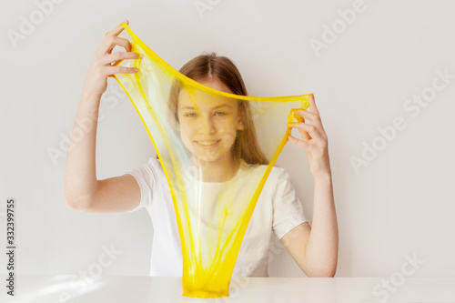 The cute girl smiles and plays with the yellow slime. The girl stretches the slime to transparency and looks through it. Slime toy, anti-stress toy