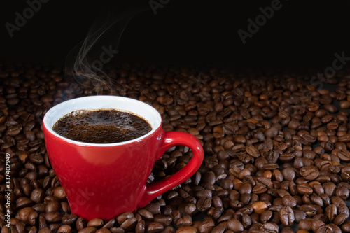 coffee in a small red cup with steam on the background of coffee beans