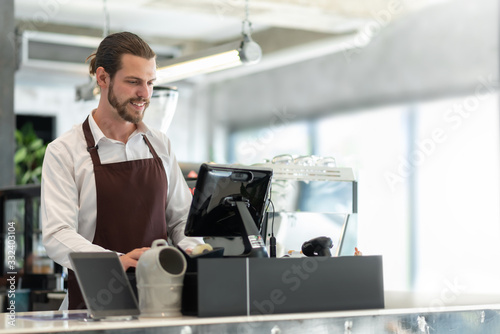 Startup of small business owner, Successful SME. Confident Male Barista working on counter at the coffee shop. Portrait of Happy smiling Bearded man wear white shirt and brown apron making coffee photo