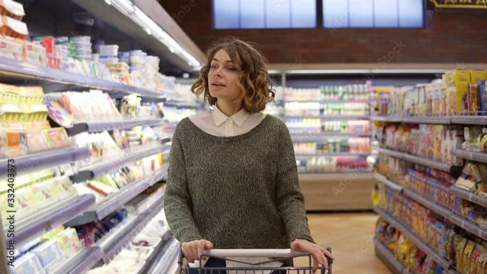 Portrait of happy, relaxful woman with curly hair went shopping with trolley cart - walk by a row and happily dancing in relaxful mood. Slow motion