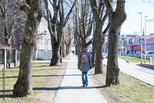 Woman walking on a sidewalk lined with trees in a hip neighborhood in Kalamaja, Tallinn on a cold spring morning