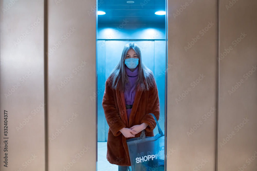 Young Asian woman in medical mask with shopping bag in elevator indoors