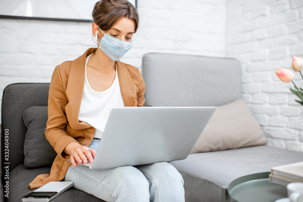 Woman in medical mask working on laptop online from home. Stay at home during a virus pandemic concept Woman in medical mask working on laptop online from home. Stay at home during a virus pandemic concept