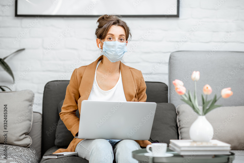 Portrait of a sad woman in medical mask working on laptop online from home. Stay at home during a virus pandemic concept Portrait of a sad woman in medical mask working on laptop online from home. Stay at home during a virus pandemic concept