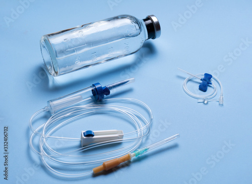glass medicine bottle with syringe injection, dropper system on blue background isolation. Close-up of an infusion system with an infusion containing a syringe containing blue liquid against a light 