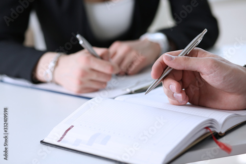 Group of people hold silver pen ready to make note in opened notebook sheet closeup. Training course, university practice homework, school or college exercise, secretary table management concept