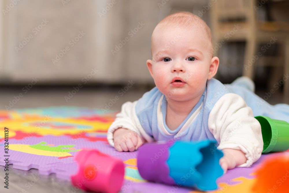 A toddler plays on the floor. The infant is lying on his abdomen on carpet with a pyramid. A toddler plays on the floor. The infant is lying on his abdomen on carpet with a pyramid.