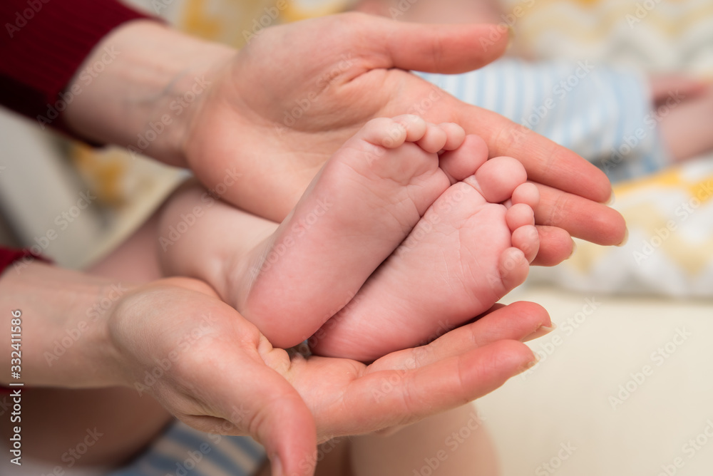 Mother's hands hold the infant's legs. The child's foots are in mom's palms. Mother's hands hold the infant's legs. The child's foots are in mom's palms.