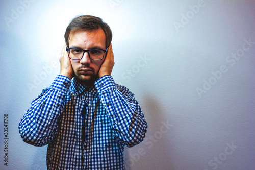Portrait young annoyed, unhappy, stressed man covering his ears, looking up, to say, stop making loud noise, giving me headache isolated on grey background with copy space. Negative emotion concept