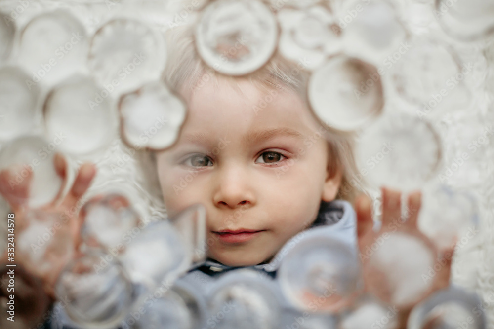 Portrait of blond toddler boy, lying under ice cubes, looking at camera Portrait of blond toddler boy, lying under ice cubes, looking at camera