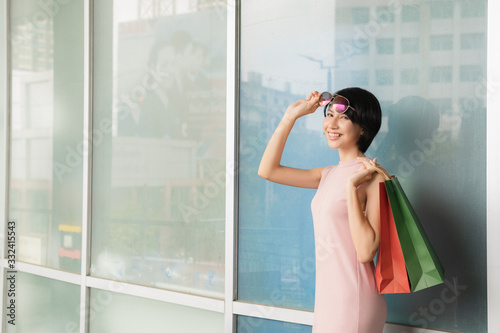 Beautiful asian shopping girl wearing pink dress, carrying a shopping bag and Leaning back on the wall