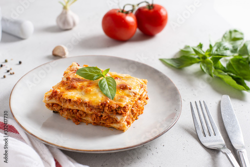 Traditional lasagna made with minced beef bolognese sauce and bechamel sauce topped with basil leaves on light background. Recipe, restaurant menu