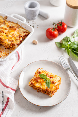 Tasty lasagna with meat and cheese on a plate, top view. Traditional italian lasagna with vegetables, basil, minced beef meat, tomato and cheese on white concrete background. Restaurant menu, recipe
