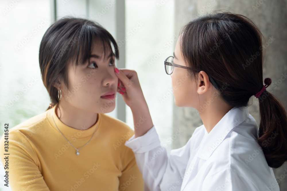female Ophthalmologist, eye doctor looking into the eye of woman patient; concept of dedicated health care worker, doctor, therapist, medical worker on the job