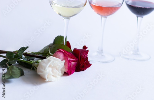 colorful rose flowers on white background with white, pink, red wine in glasses