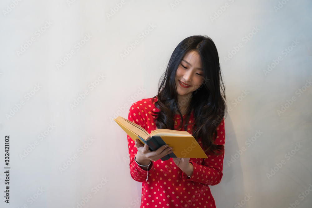 Portrait of young female student standing reading a book in front of the wall Portrait of young female student standing reading a book in front of the wall