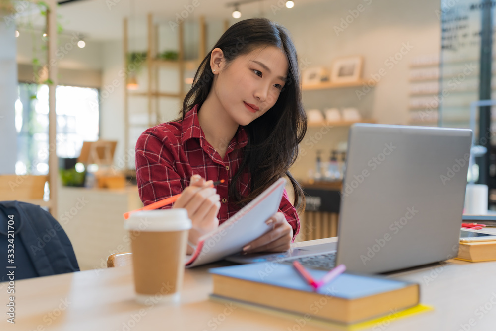 Close up of young business woman sitting while holding orange pen and notebook in her hands at table, and watching notebook Close up of young business woman sitting while holding orange pen and notebook in her hands at table, and watching notebook