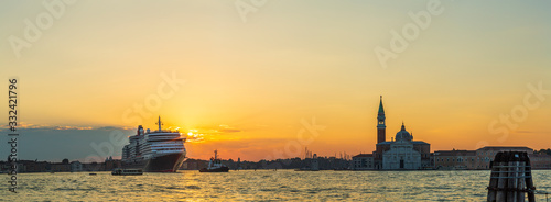 A tugboat at sunrise guides a huge cruise liner along a canal in Venice