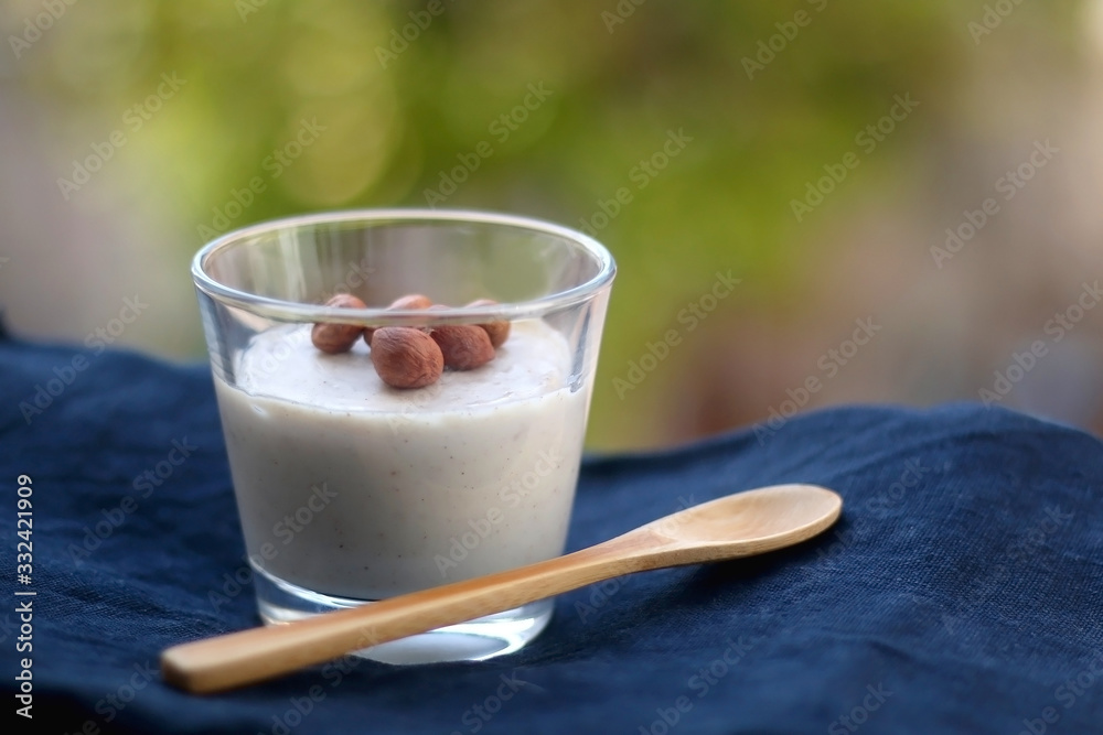 Glass of vanilla pudding with hazelnut topping and wooden spoon. Selective focus. Glass of vanilla pudding with hazelnut topping and wooden spoon. Selective focus.