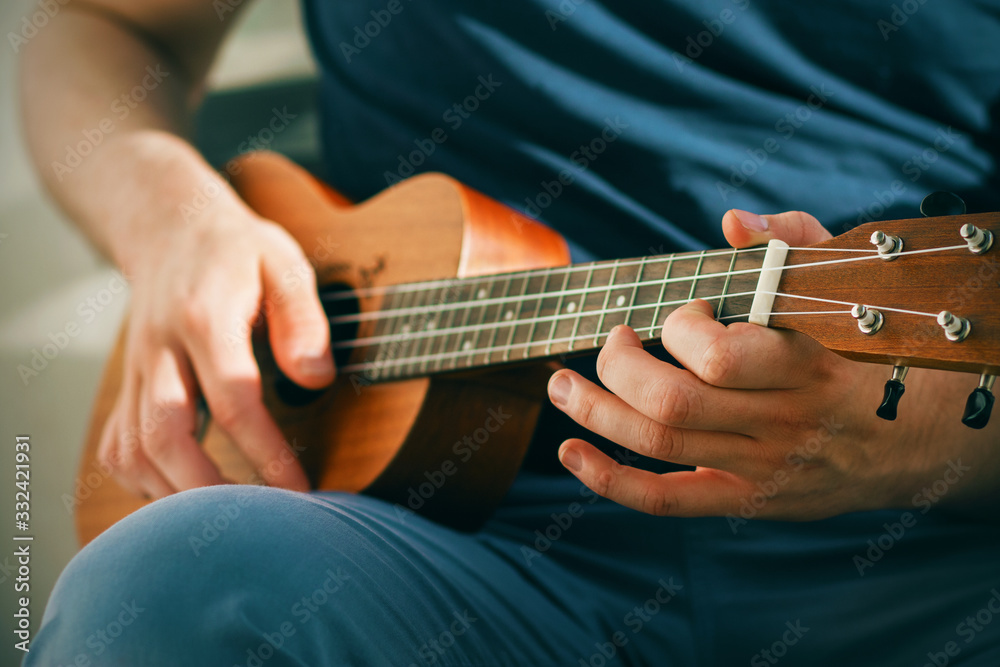 A musician in blue clothes plays a cheerful tune on a small ukulele on a Sunny day.