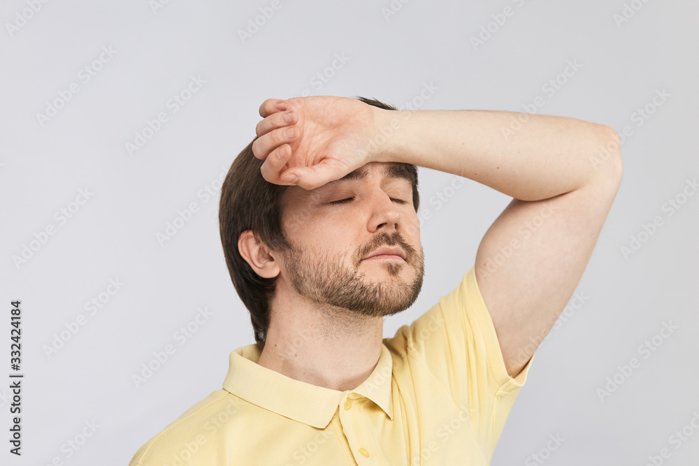 strong young man touching his forehead with arm to check his body temperature isolated on grey background strong young man touching his forehead with arm to check his body temperature isolated on grey background
