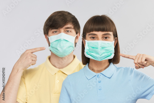 young couple in protective facial mask looking to the camera and pointing on it