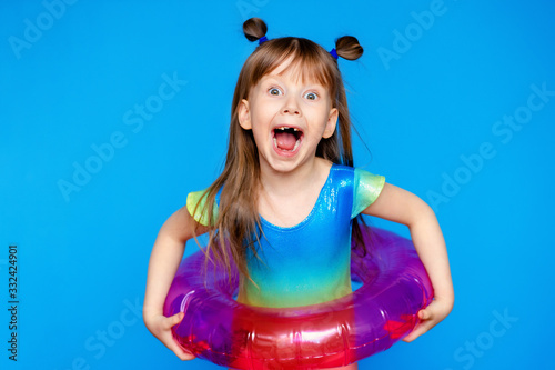 little cute girl child in a swimsuit with a swimming circle on a blue background