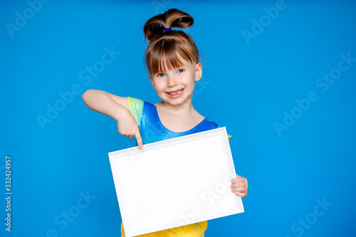 Girl holding a white sheet. Cute little girl with a white sheet of paper.blue background.space for text.