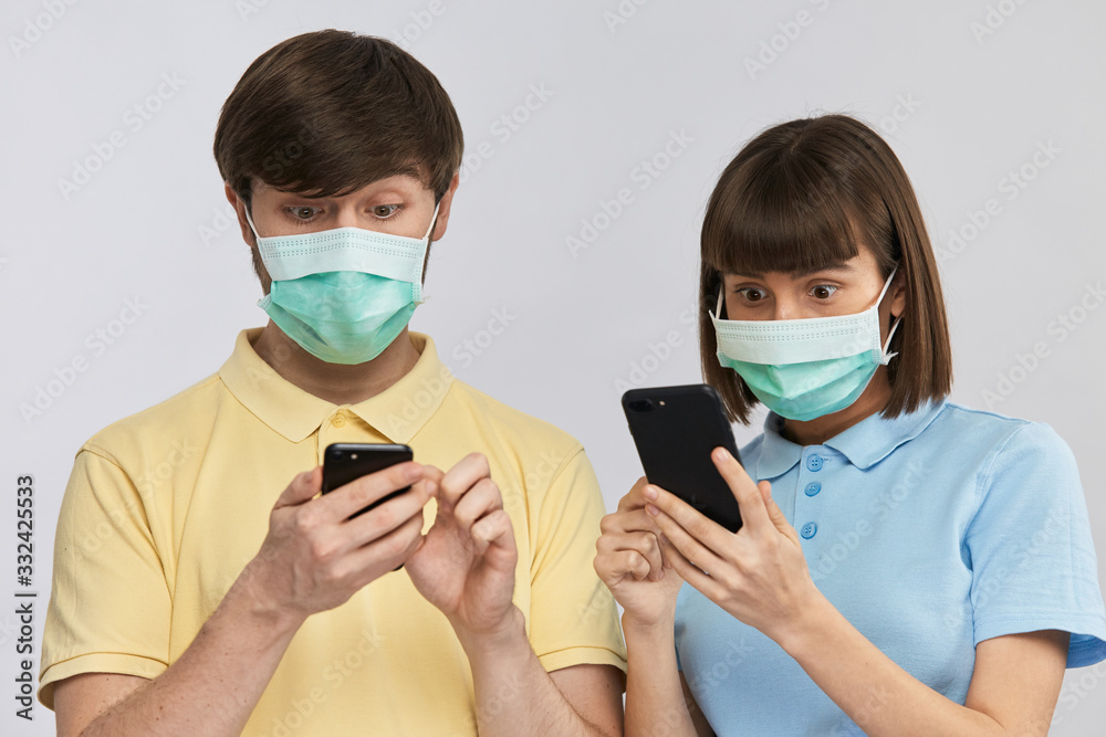 terrified man and woman looking to phones wearing protective antipandemic masks