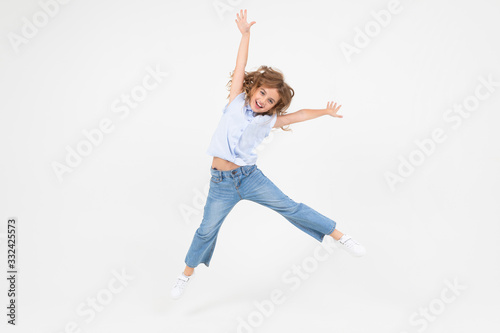 young girl in jeans jumping with happiness on a white background with copy space