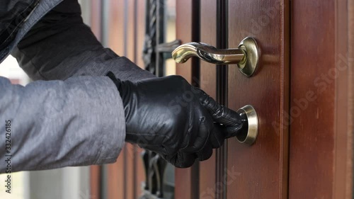 a thief in gloves opens the door lock of a private house and penetrates inside in broad daylight