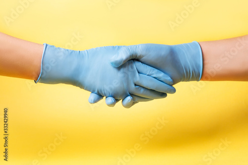 Women's hands in blue medical gloves on a yellow background Handshake Coronovirus concept
