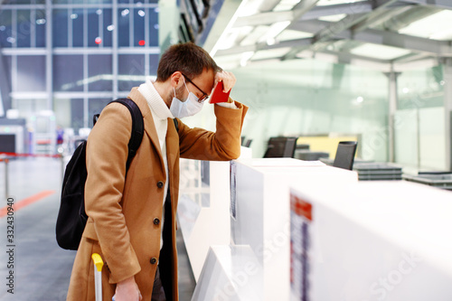 Man in mask stuck in empty airport in coronavirus quarantine isolation, waiting for departure, flight cancellation, pandemic infection worldwide spread, travel restrictions and border shutdown photo