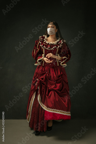 Medieval young woman as a duchess wearing protective mask against coronavirus spread on dark blue background. Concept of comparison of eras, healthcare, medicine and prevention against pandemic.