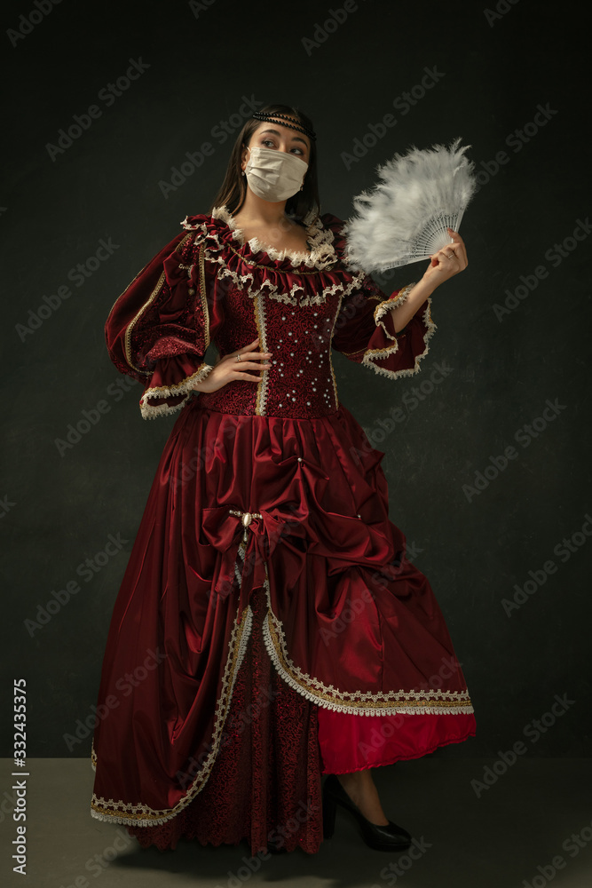 Medieval young woman as a duchess wearing protective mask against coronavirus spread on dark blue background. Concept of comparison of eras, healthcare, medicine and prevention against pandemic.