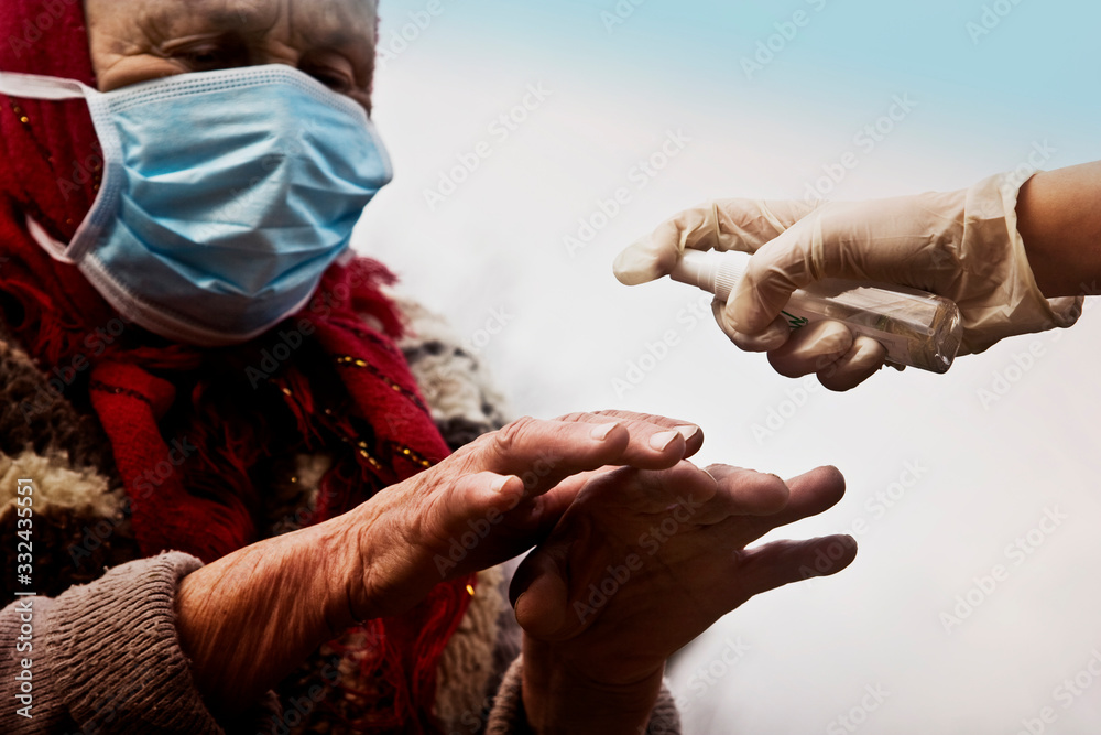 An old grandmother in a mask disinfects her hands with an antiseptic. An old woman disinfects her hands with an antiseptic to prevent coronavirus infection. Sanitary measures for an outbreak of corona