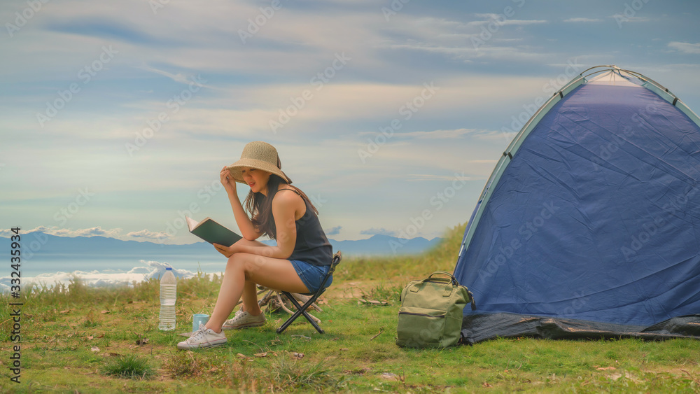 Young woman tourist sitting near the tent and reading a book
