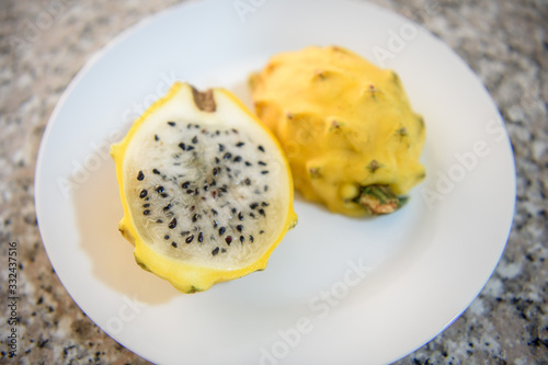 Top view photo with shallow depth of field of a yellow dragon fruit cut in half on a white ceramic plate.