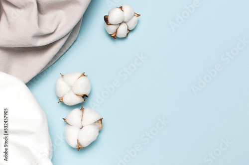 White gray crumpled natural cotton fabric and cotton flowers on delicate blue background top view flat lay copy space. Natural linen background. Eco textiles. White Fabric texture. Fabric backdrop