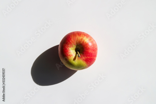 Fresh apple with strong shadow on white background at sunny day. Trendy minimal food concept. Organic natural fruit