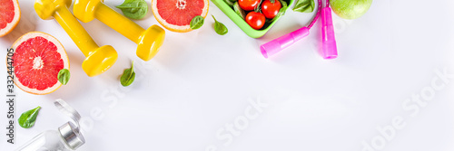 Fitness and healthy food lifestyle concept. Dumbbells, diet fruit and vegetable lunch box, water and jump rope on white background. Flatlay image, top view copy space