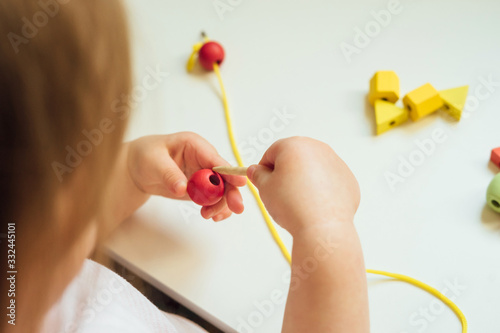 Child putting beads on a string. Bead stringing activity. Fine motor skills development. Lacing, threading. photo