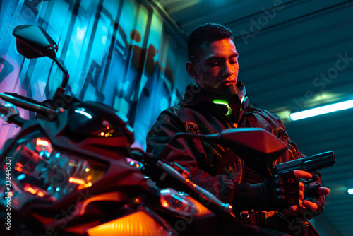 selective focus of bi-racial cyberpunk player near motorcycle looking at gun © LIGHTFIELD STUDIOS