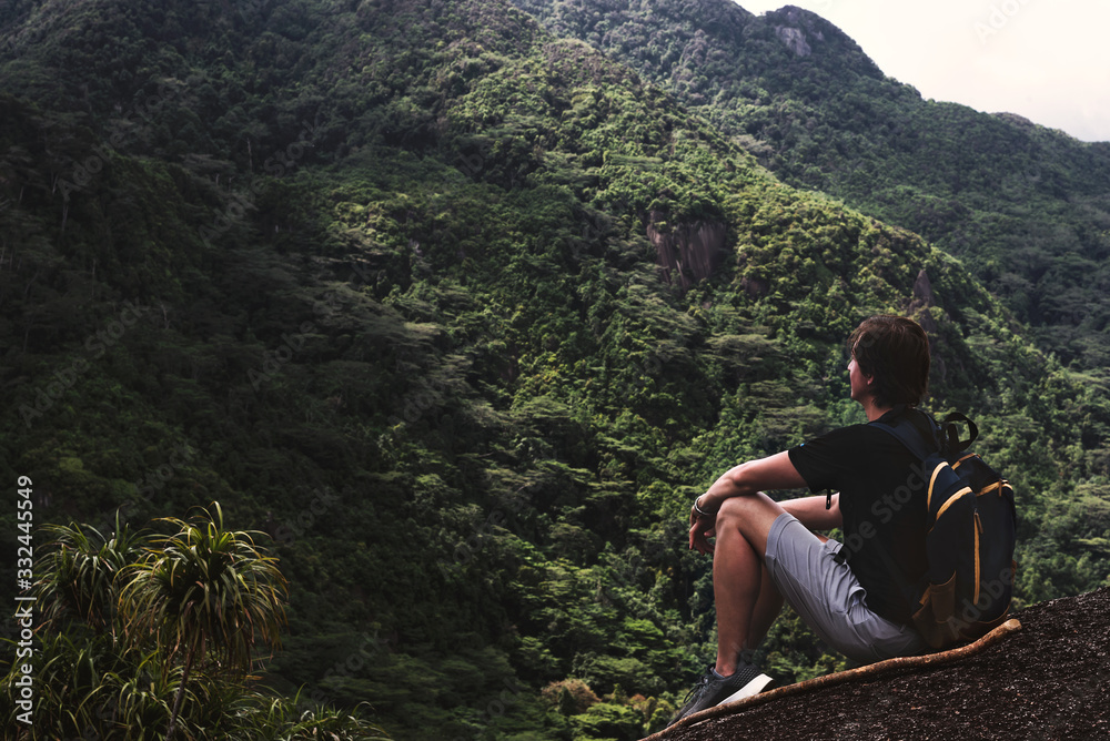 Young man resting on top of the mountain and looking at breathtaking view Young man resting on top of the mountain and looking at breathtaking view
