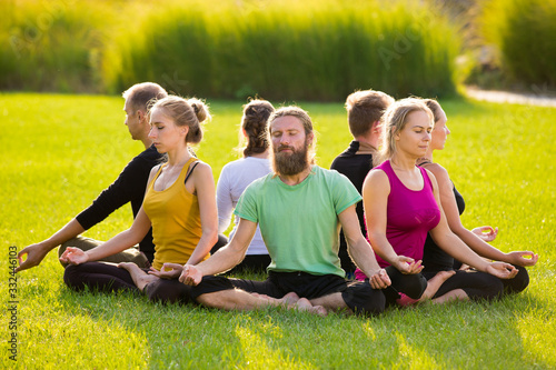 A group of people in a lotus pose on a green lawn in the park © artem_goncharov