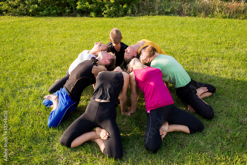 A group of people in a lotus pose on a green lawn in the park