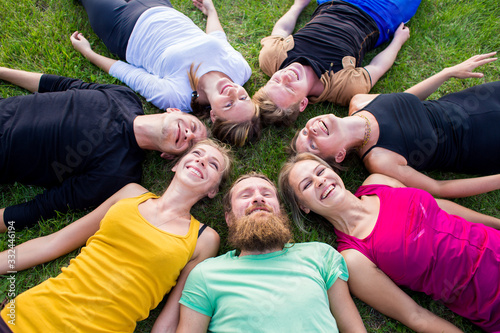 A group of people lies on a green grass in a circle