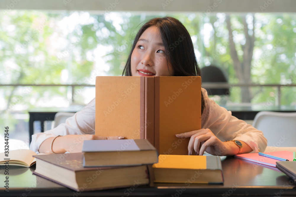 Beautiful student wearing white shirt reading books on the table in library Beautiful student wearing white shirt reading books on the table in library